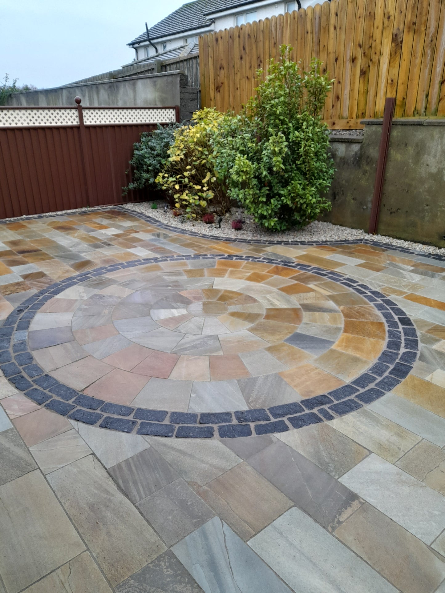Mosaic stone patio with circular pattern and green plants in the background. Patio border created using 20mm Gold Donegal Quartzite Stone Chipping.