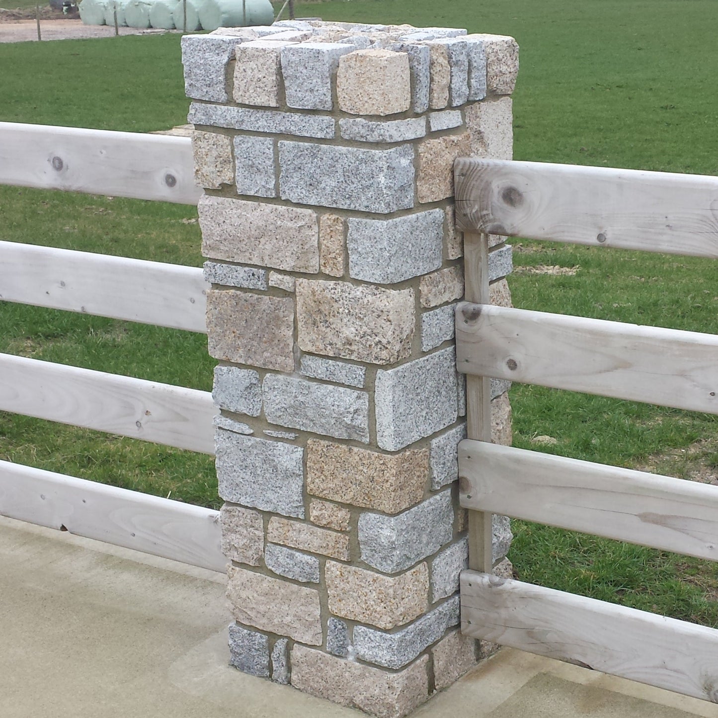 Stone pillar in Donegal Granite with wooden fence in a field.