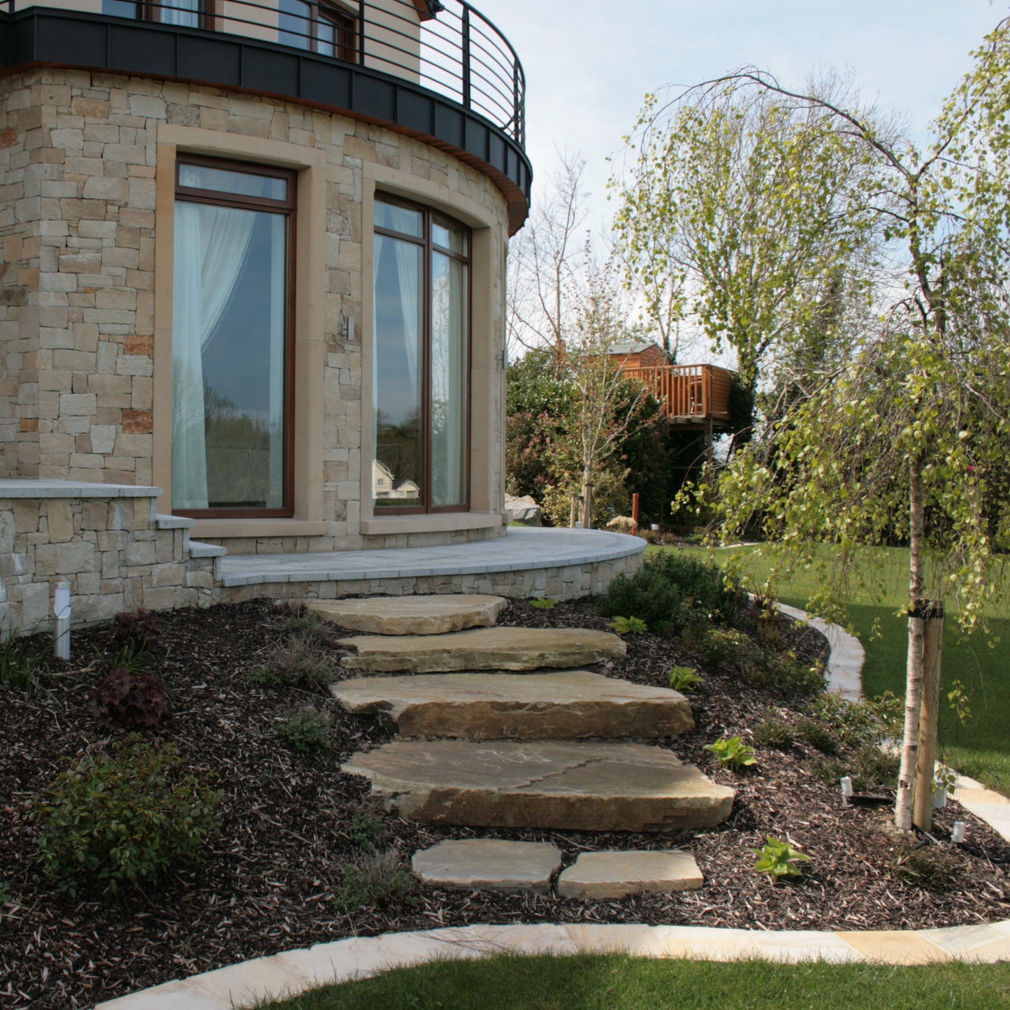 Stone steps leading up to a house with stone facade and large windows.