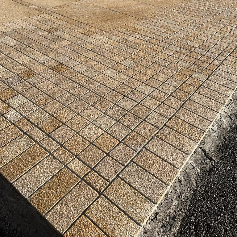 Paved patio area with a house in the background. Two cobble sizes with the outer border featuring Sawn Gold Granite in 200 x 100mm size.