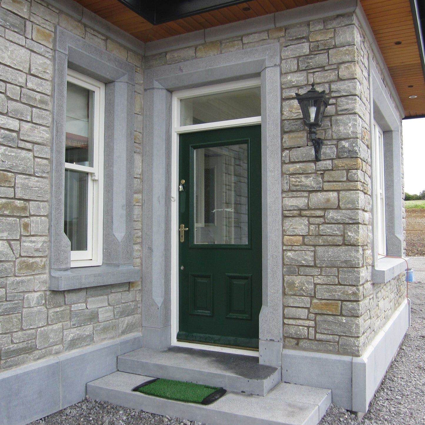 Green door of a house with stone facade with bespoke blue limestone door and window surrounds.