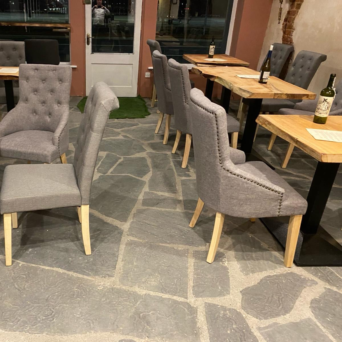 A seating area with wooden tables and chairs, featuring grey upholstered backrests and seats, on a floor made of Liscannor Slate Crazy Paving stone with a textured, non-slip surface.