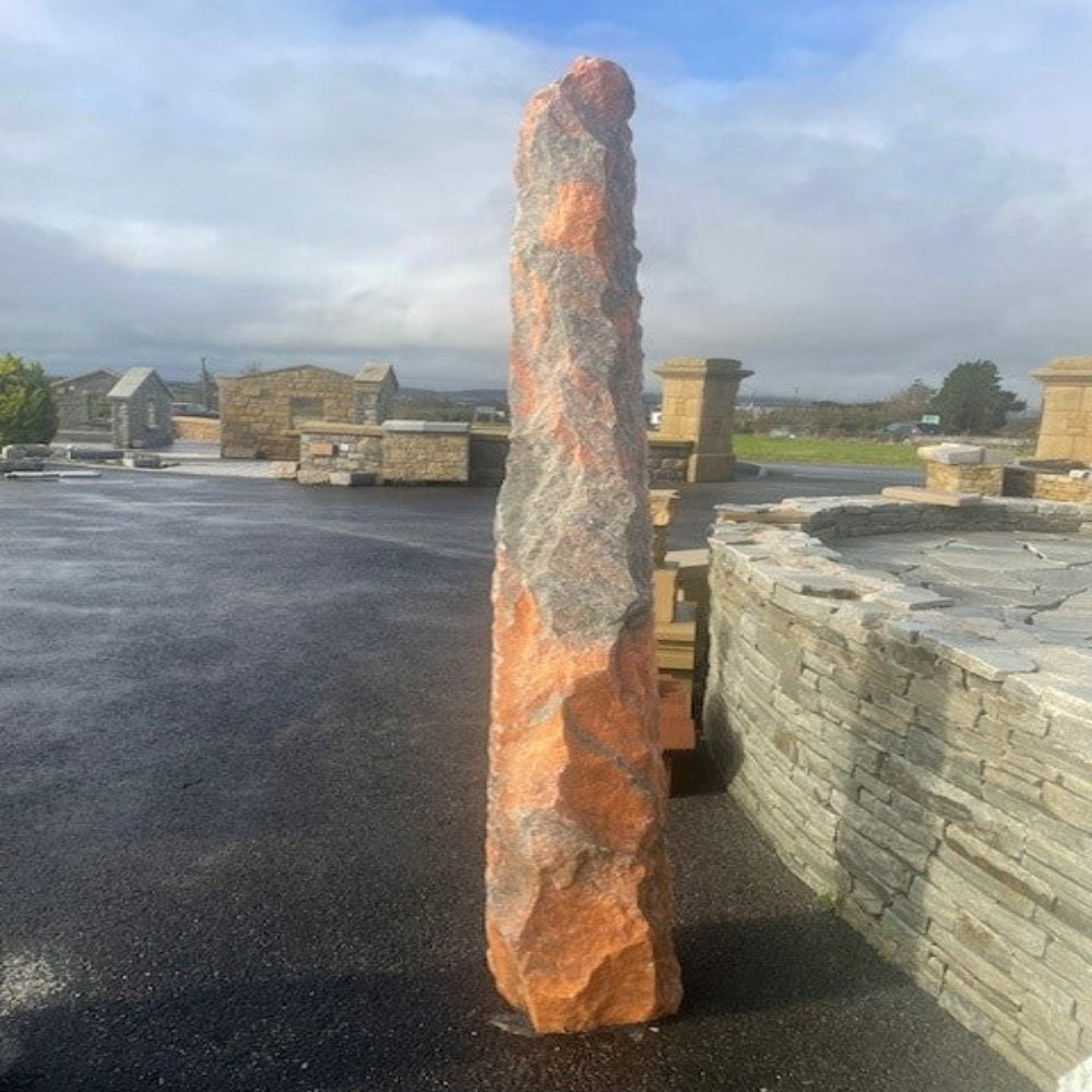 Tall pink marble monolith with a textured surface in an outdoor setting