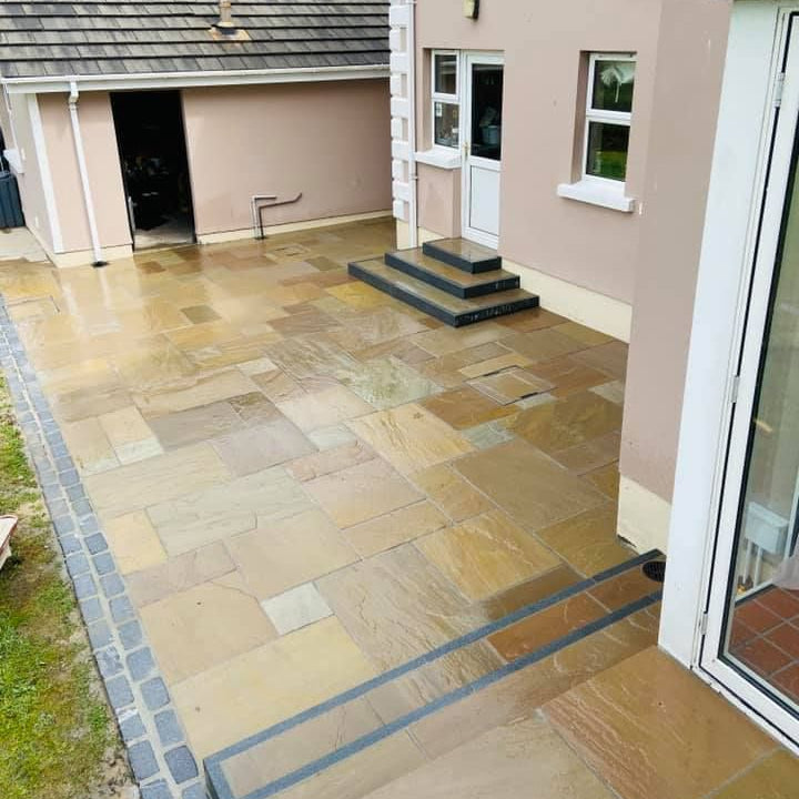 Paved patio area leading to a house with a door and windows. Paving installed is Raj Green Sandstone in Patio Pack sizes.