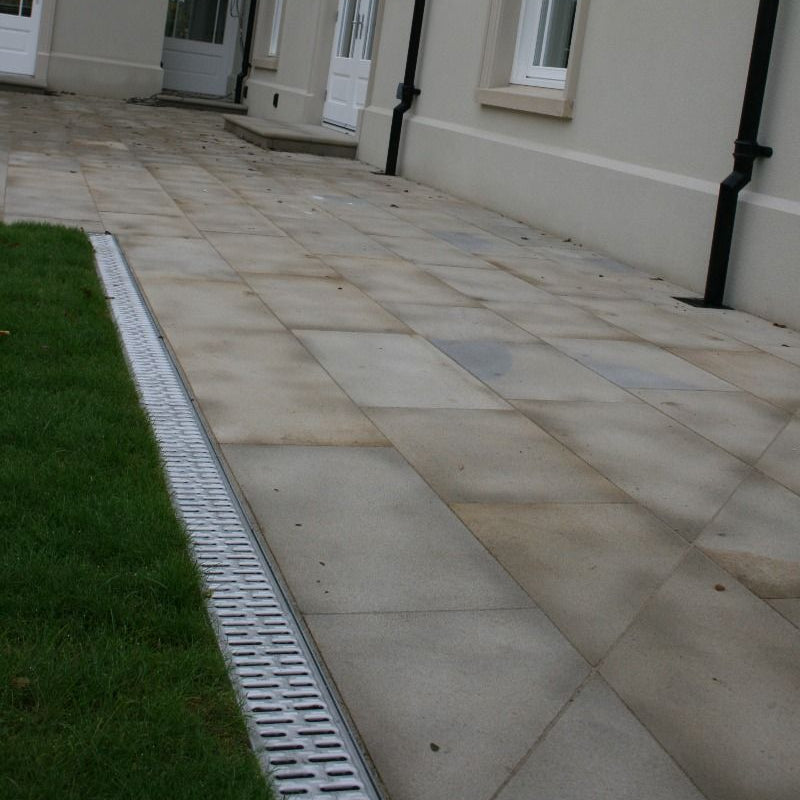 Galvanised STORA Light Channel Drain installed in a patio area featuring Mountcharles Sandstone Paving.