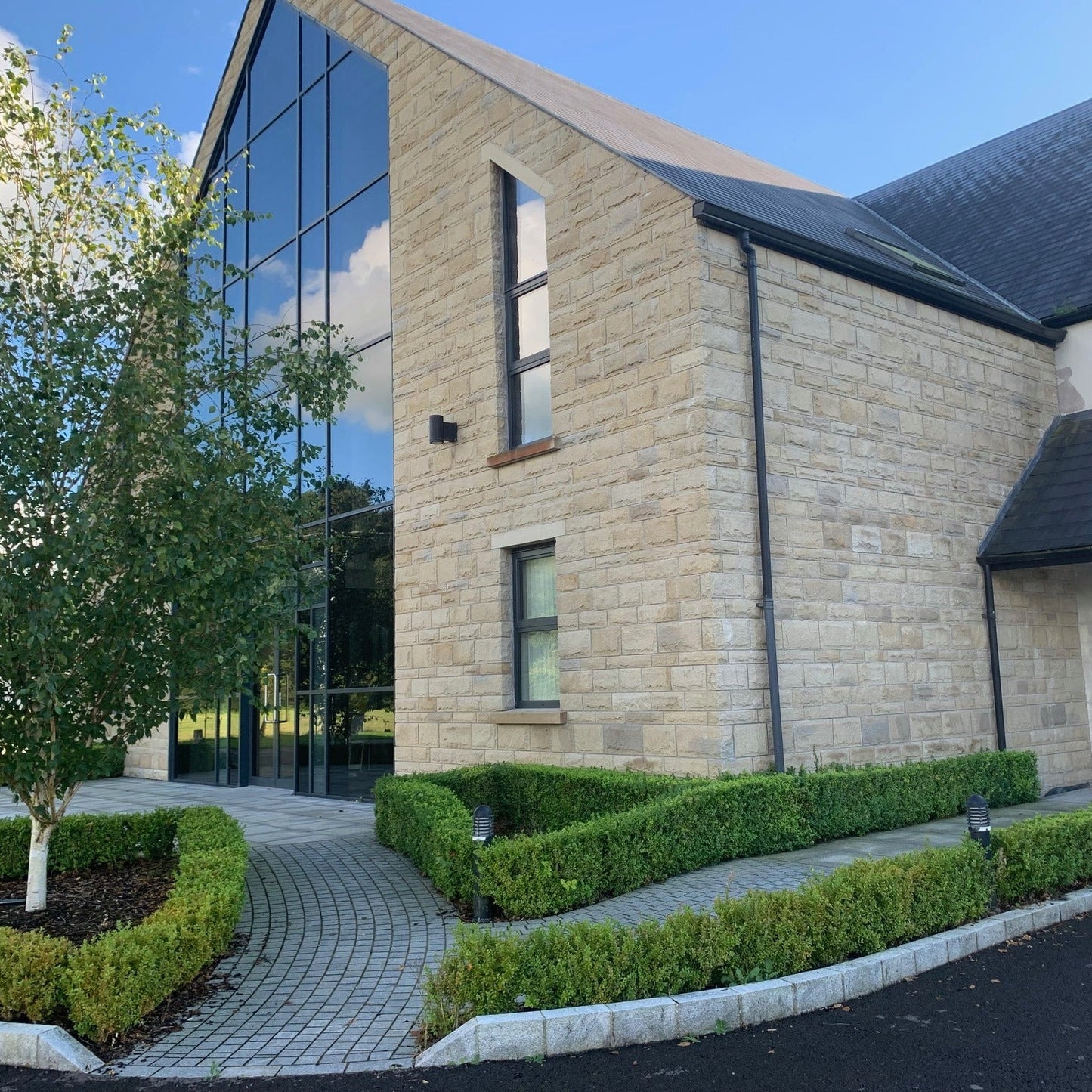 Large architectural building with large glass windows with smaller windows featuring bespoke sandstone lintels and sills.
