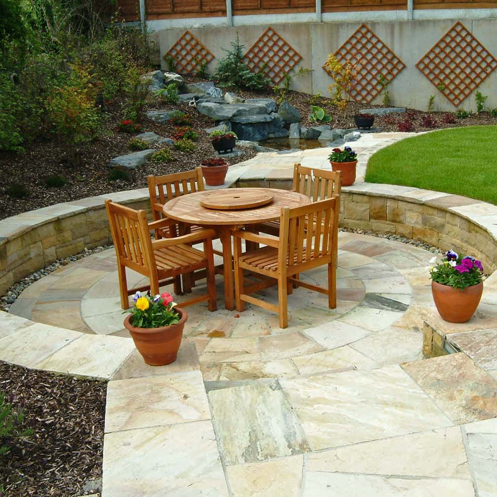 Outdoor patio with wooden furniture and decorative elements. Patio features a 4m Tinted Mint Sandstone Paving Circle.