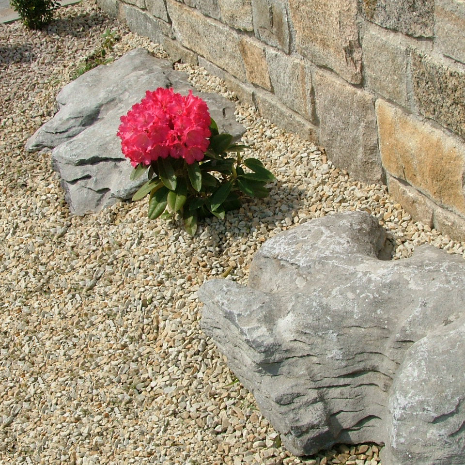 Pink flower in a garden with stone wall and decorative rocks surrounded by 10mm Gold Donegal Quartzite Stone Chipping. 
