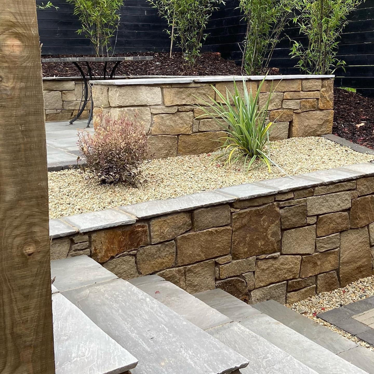 Outdoor garden scene with stone wall, steps, and plants in bed of 10mm Gold Donegal Quartzite Stone Chipping. 