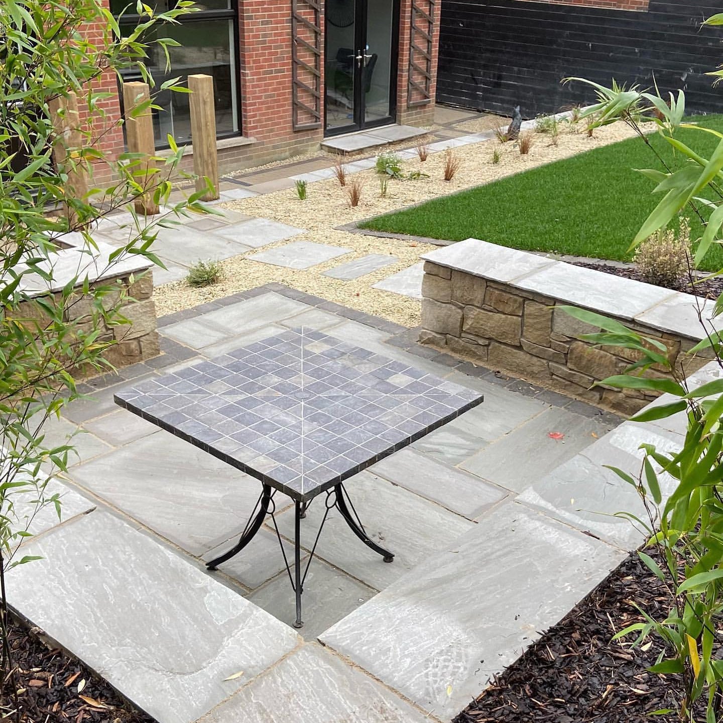Patio area with a square table in a garden setting, featuring stone pavement and greenery. Pathway created using 10mm Gold Donegal Quartzite Stone Chipping. 
