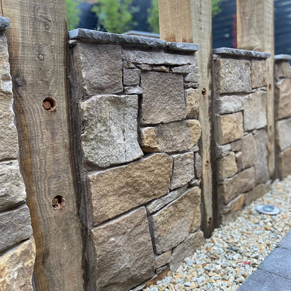 Stone wall with wooden posts in a garden setting bordered by 10mm Gold Donegal Quartzite Stone Chipping. 