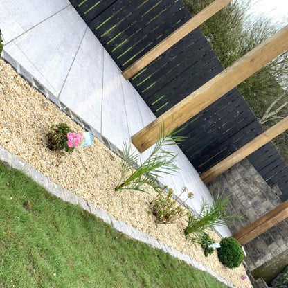 Garden bed with plants and 10mm Gold Donegal Quartzite Stone Chipping gravel next to a patio and wooden fence. 