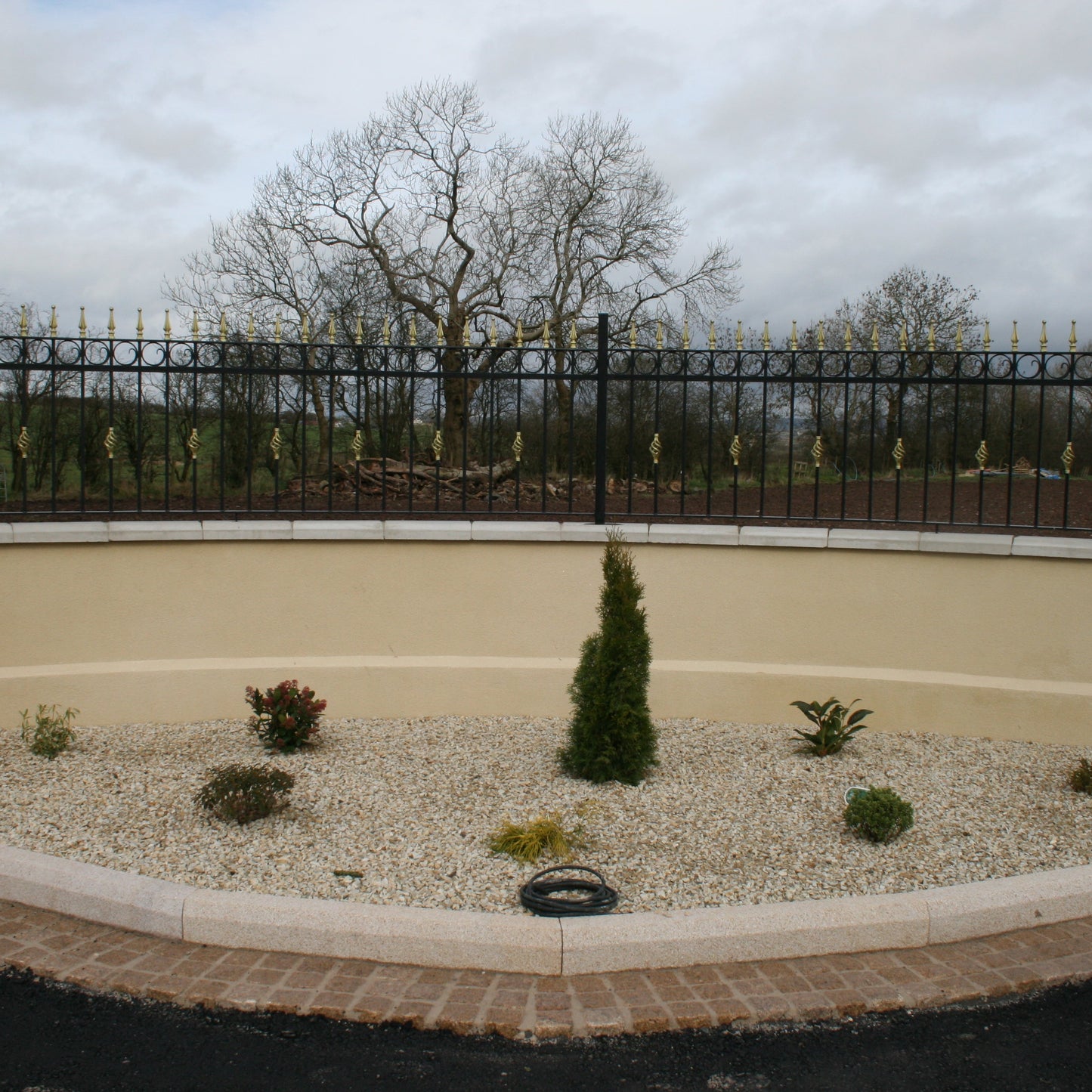 Boundary wall with black railing with trees in the background. Planted flower bed features 14mm Gold Donegal Quartzite Stone Chipping.