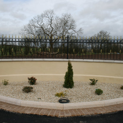 Boundary wall with black railing with trees in the background. Planted flower bed features 14mm Gold Donegal Quartzite Stone Chipping.