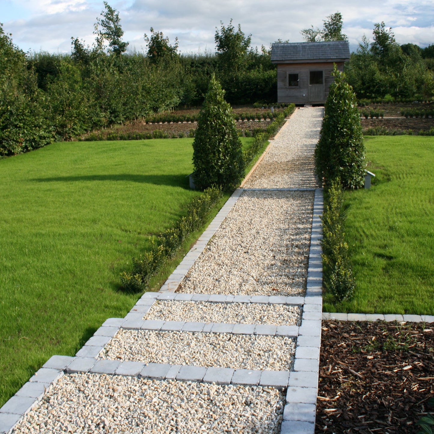 Garden pathway featuring 14mm Gold Donegal Quartzite Stone Chipping leading towards a wooden shed. 