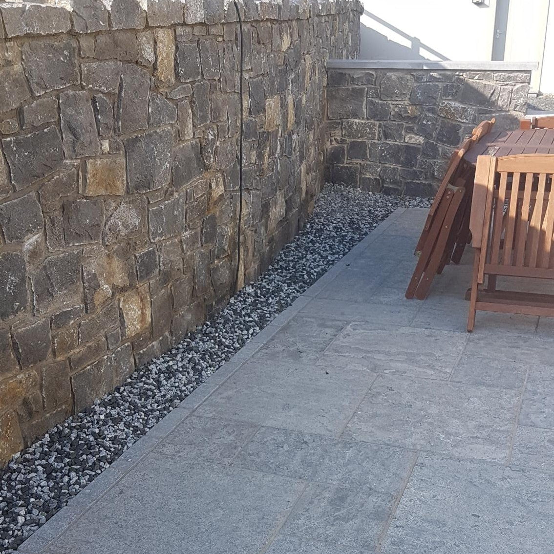 Paved pathway leading to a stone wall with a wooden bench on a patio.