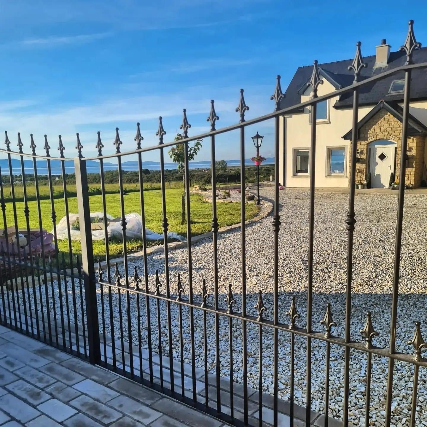 Wrought iron gate leading to a driveway with a house in the background. Driveway completed using 20mm Gold Donegal Quartzite Stone Chipping.