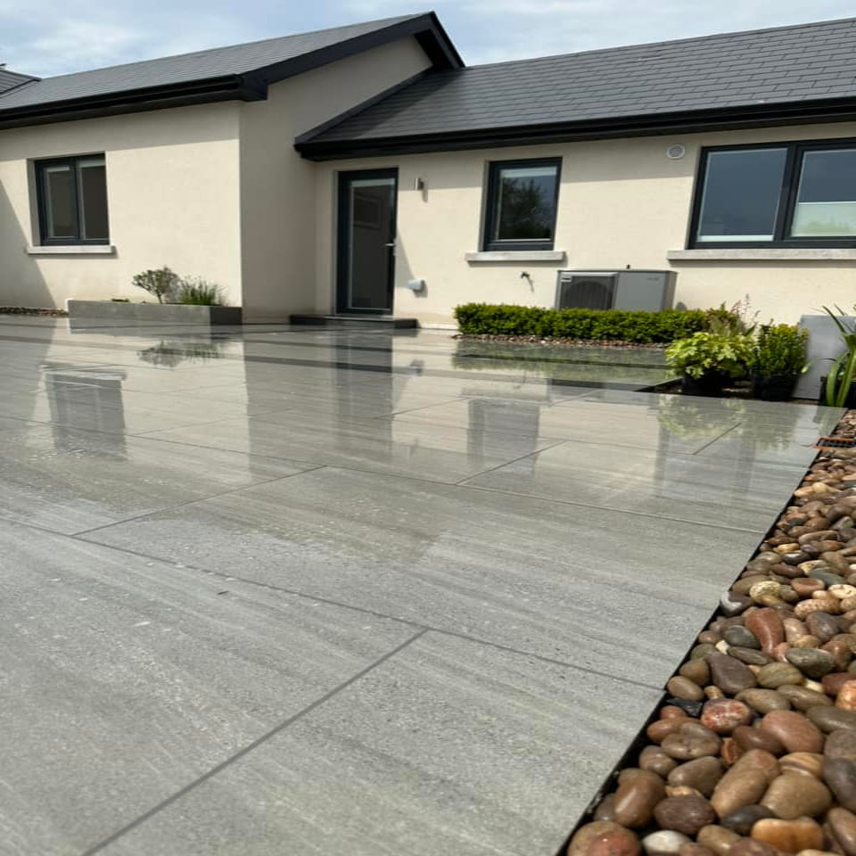 Ashen Jewel Range Porcelain Paving Tiles installed on the ground, showing a modern and sleek appearance with a house and garden in the background.