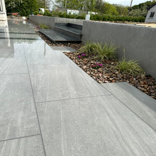 An outdoor installation of Ashen porcelain paving tiles in a garden setting, with a grey colour. 
