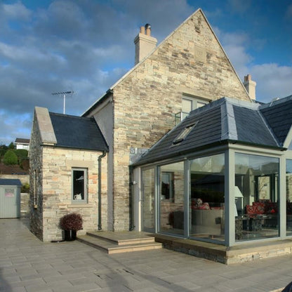 Stone house with a glass extension on a cloudy day. Stone is Atlantic Grey Donegal Quartzite Machined. 