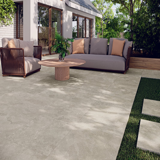 Outdoor patio with grey sofa, chairs, and table on a patio completed using Street Beige porcelain paving tiles. 
