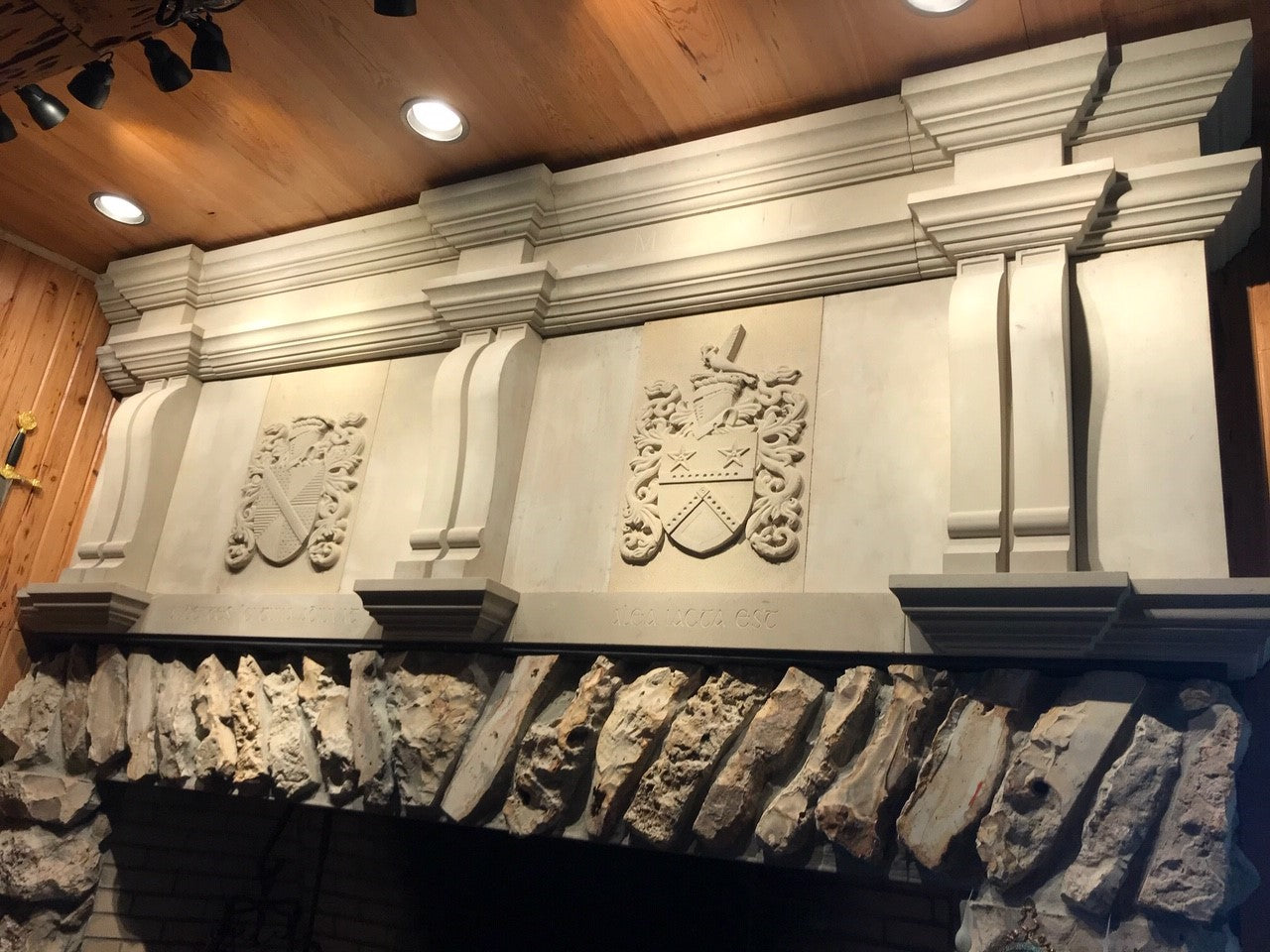 Architectural Sandstone Mantel with two craved family crests above a large natural stone fireplace. 