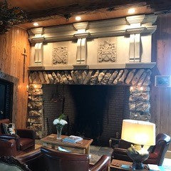 Architectural Sandstone Mantel including cravings of two family crests. Mantel sits above a large stone fireplace in a living room. 