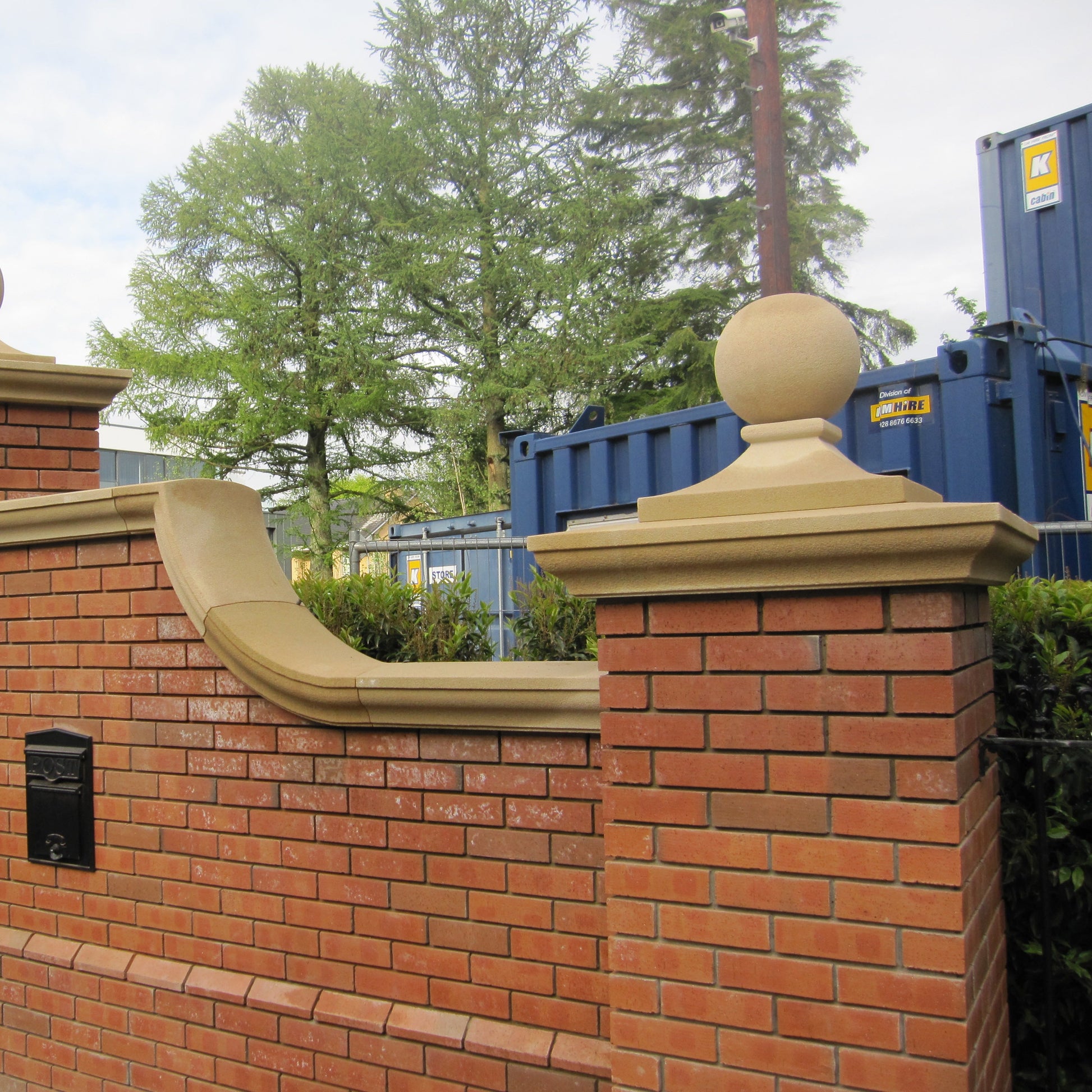 Red brick entrance wall with bespoke sandstone pillar caps with spheres on top. 