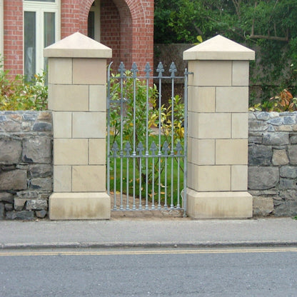 Bespoke sandstone gate pillars with bespoke apex sandstone pillar caps. Red brick house in the background. 