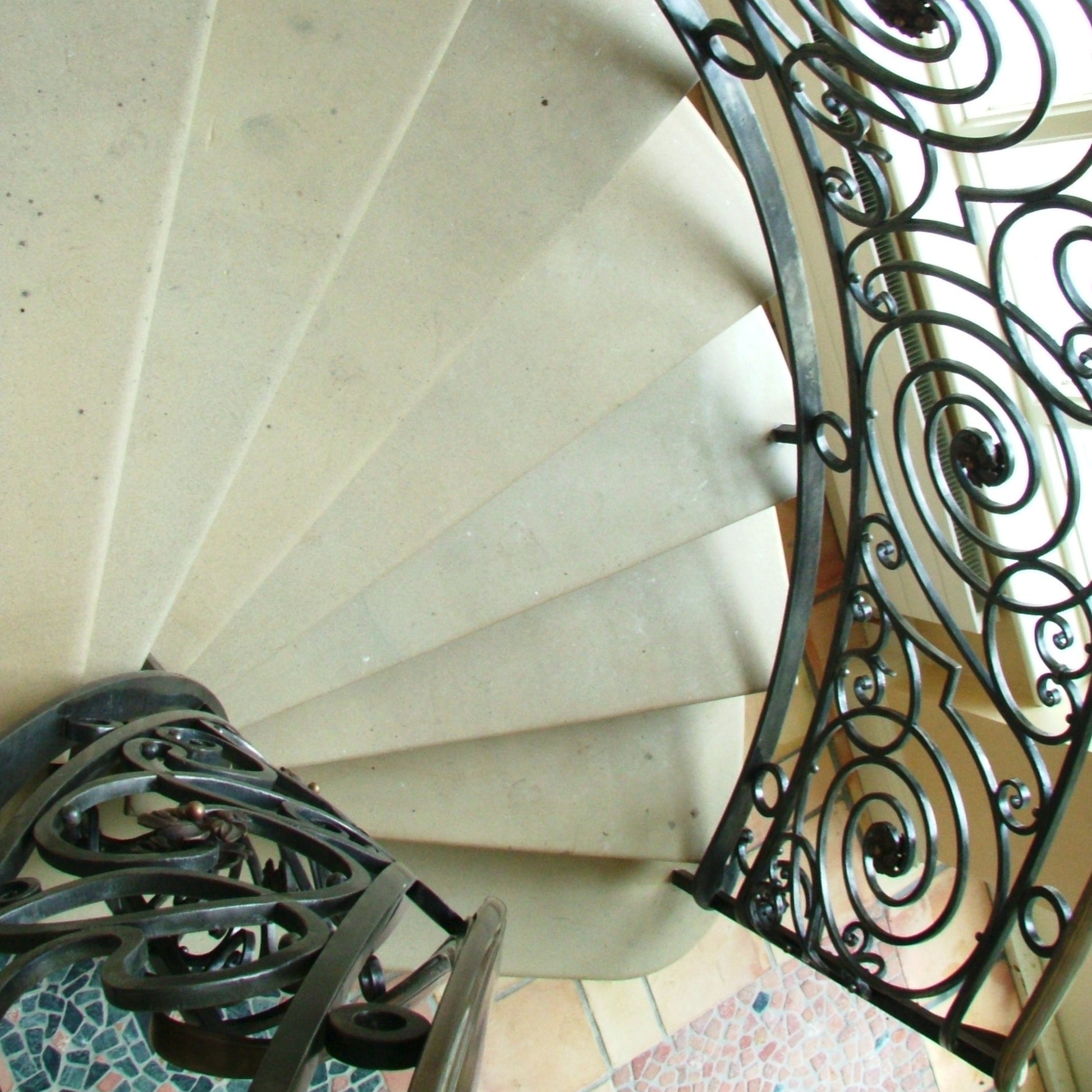 Spiral sandstone staircase with decorative metal railing in a well-lit interior setting