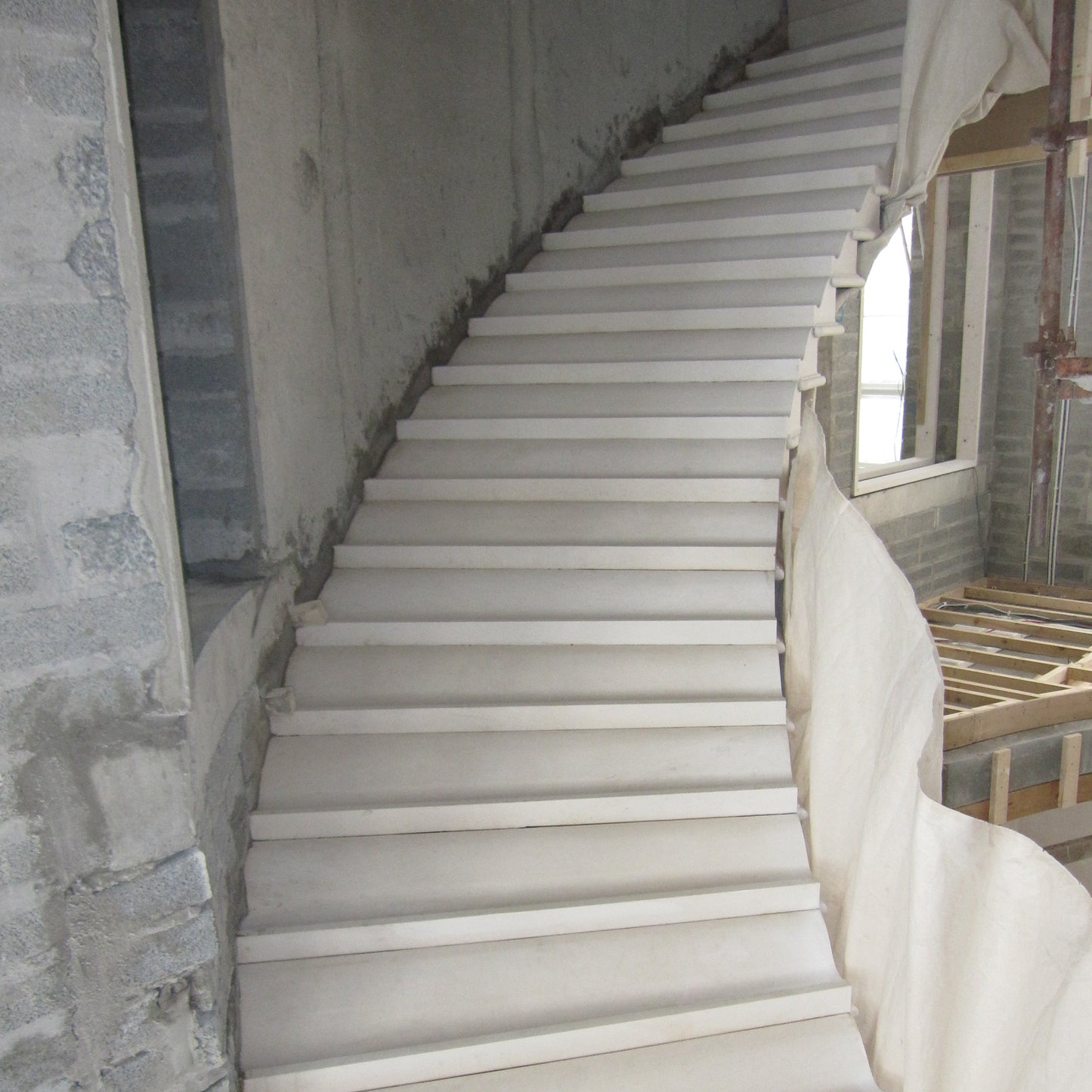 Architectural Sandstone staircase in a building under construction with exposed concrete walls.