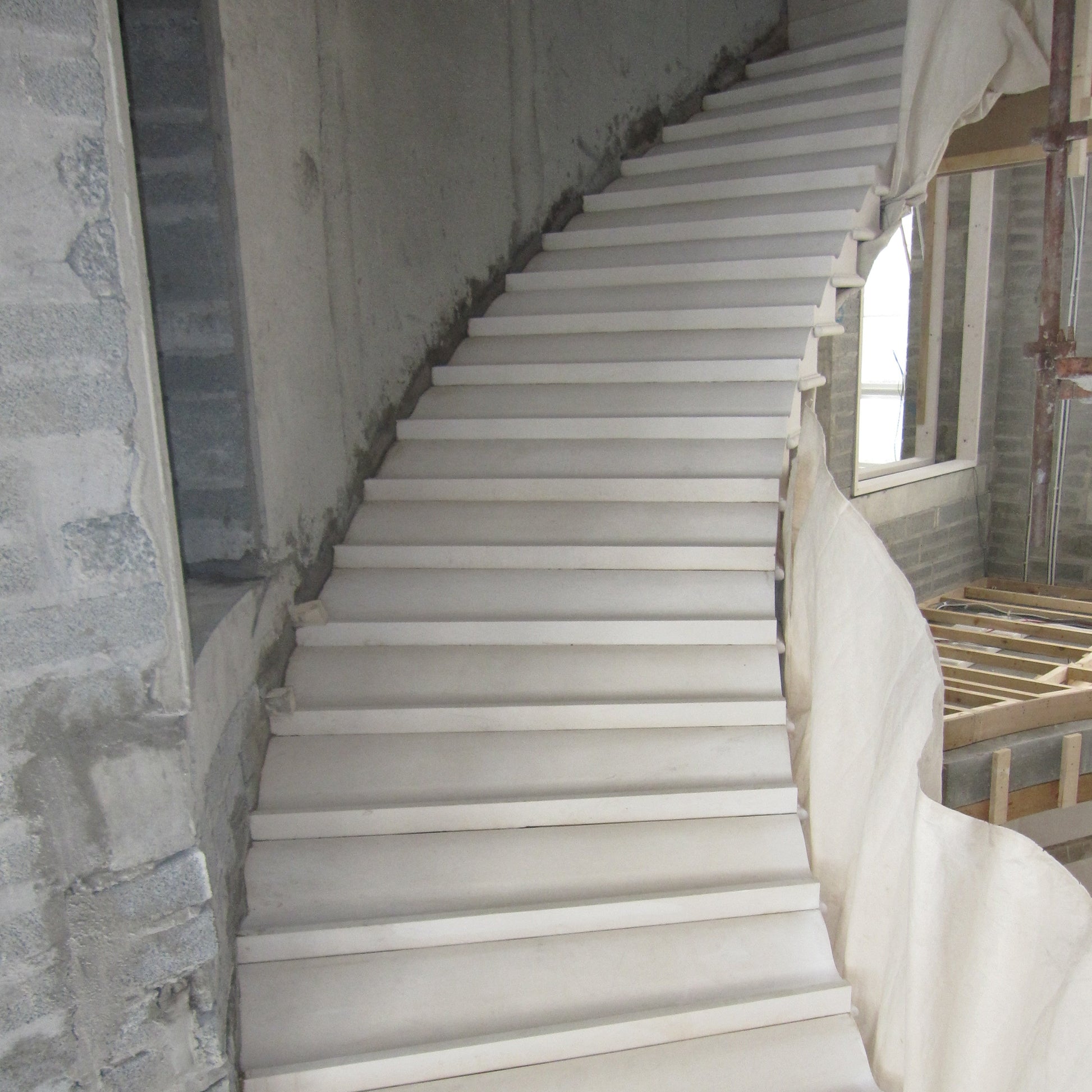 Architectural Sandstone staircase in a building under construction with exposed concrete walls.