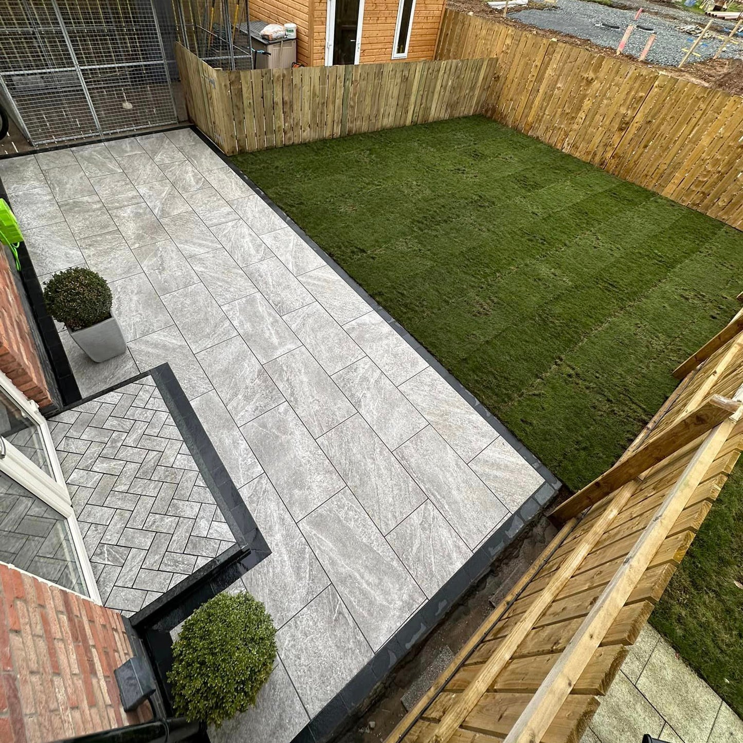 Backyard with porcelain patio, grass area, and wooden shed. Patio step surrounded by Black Granite Kerbing. 