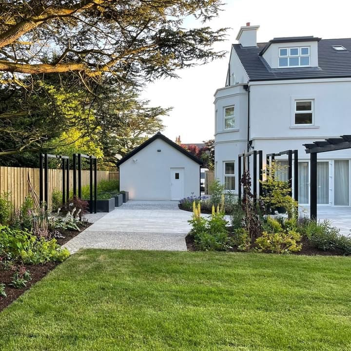 White house with a well-maintained garden and trees. Patio features Black Granite Cobbles.