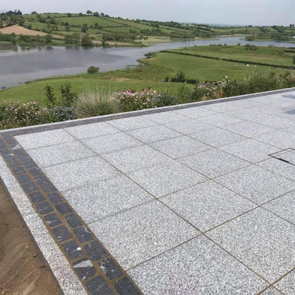 Paved area with a scenic view of a lake and green fields. Patio border completed using Black Granite Cobbles in 200 x 100mm. 