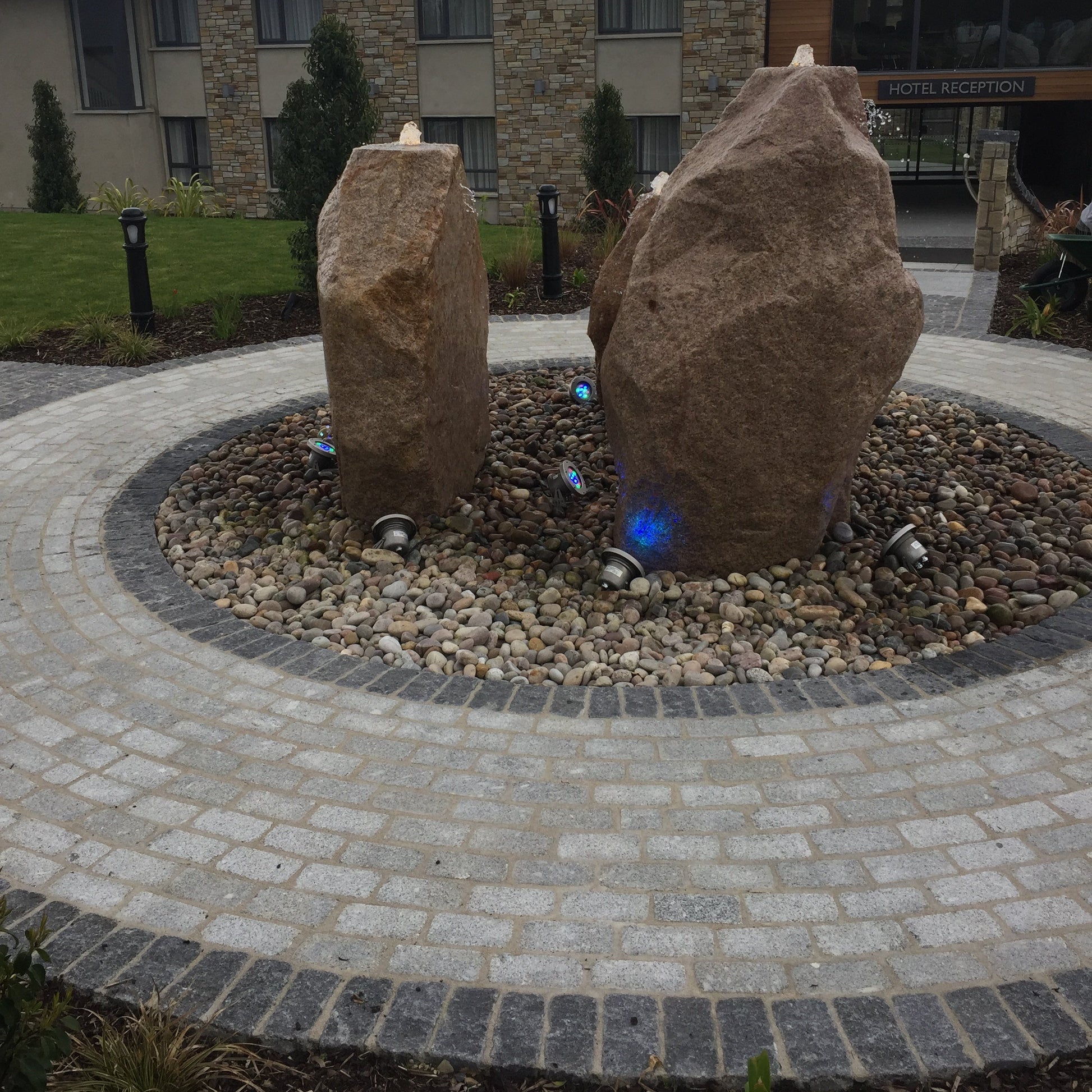 Stone monoliths in a circular stone pathway completed using Silver & Black Granite Cobbles in 200 x 100mm with a building in the background.