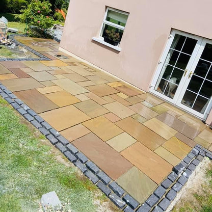 Paved patio area using Raj Green Sandstone Paving and Black Granite Cobbles in front of a house with a garden