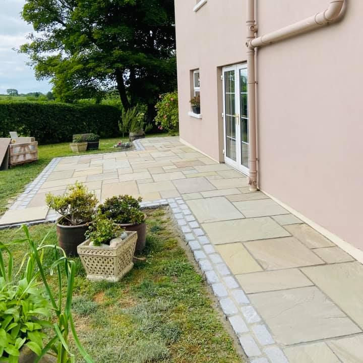 Patio area with potted plants in front of a house. Paving is Raj Green Sandstone Patio Packs & Black Granite Cobbles in 200 x 100mm. Photographed dry. 