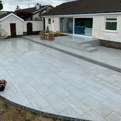Modern porcelain paved patio with Black Granite Cobble border in front of a house with outdoor furniture