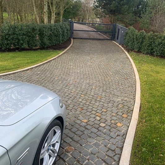 Silver car parked on a cobblestone driveway leading to a gate. Paving is Black Granite Cobbles in 100 x 100mm size. 
