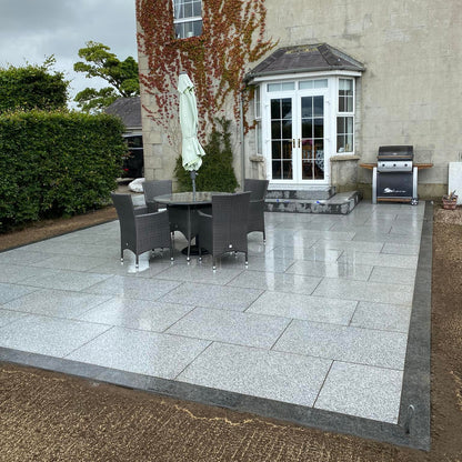 Paved patio area in front of a house with outdoor furniture and grill. Patio border completed using Silver Granite Pin Kerbs. 