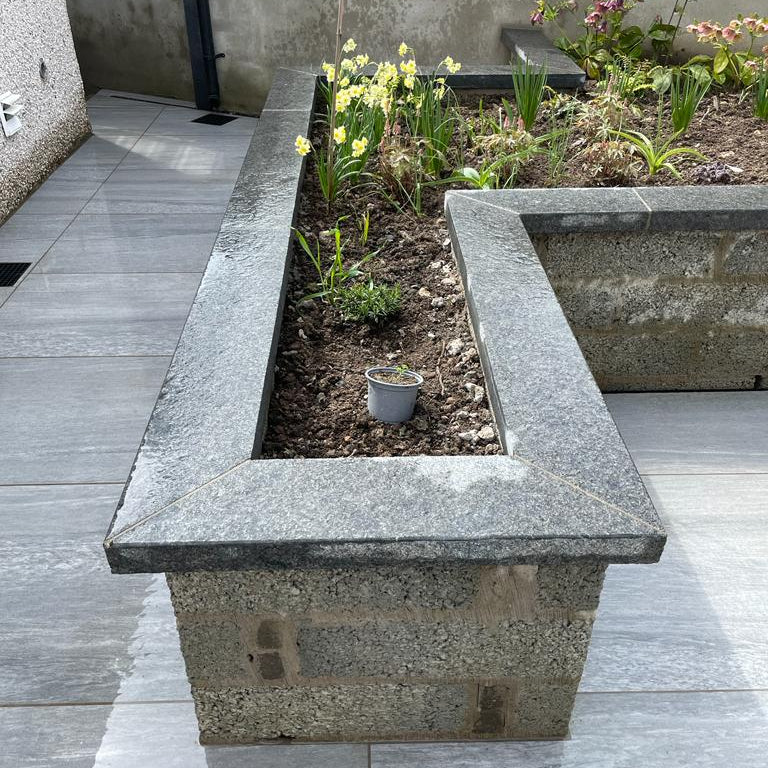 Concrete planter with flowers on a patio. Planters feature Black Granite Wall Capping.