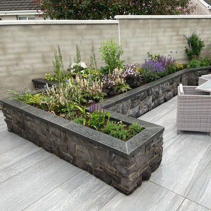 Outdoor porcelain patio with stone planters completed with bespoke Black Granite Wall Capping.