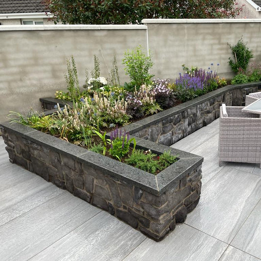 Outdoor porcelain patio with stone planters completed with bespoke Black Granite Wall Capping.