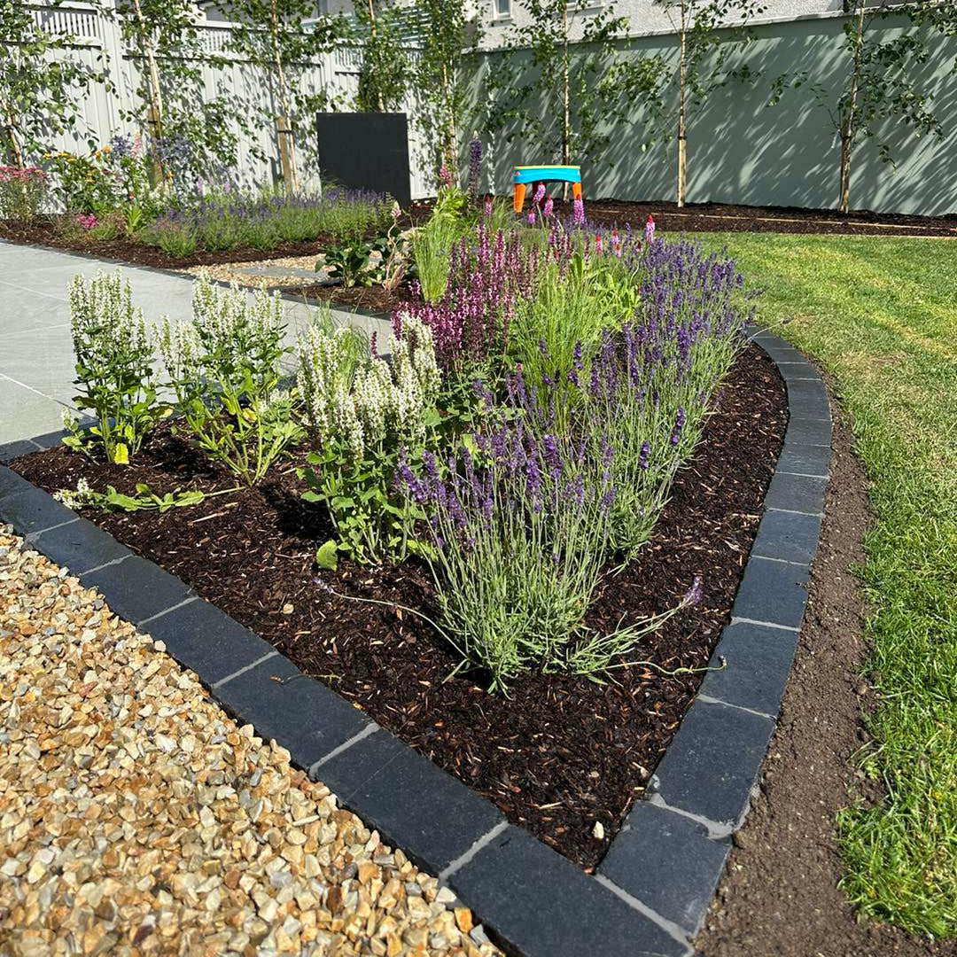 Garden with flower bed surrounded by Black Limestone Paving Cobbles in 200 x 100mm size.