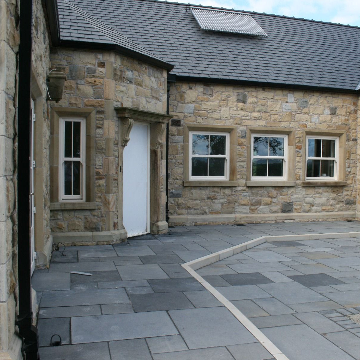 Stone house with white windows and door. Paving is Black Limestone Paving in patio pack sizes. 