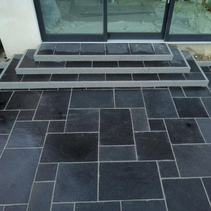 Black limestone patio slabs arranged on the ground in a pattern, with a set of steps leading up to patio doors. 