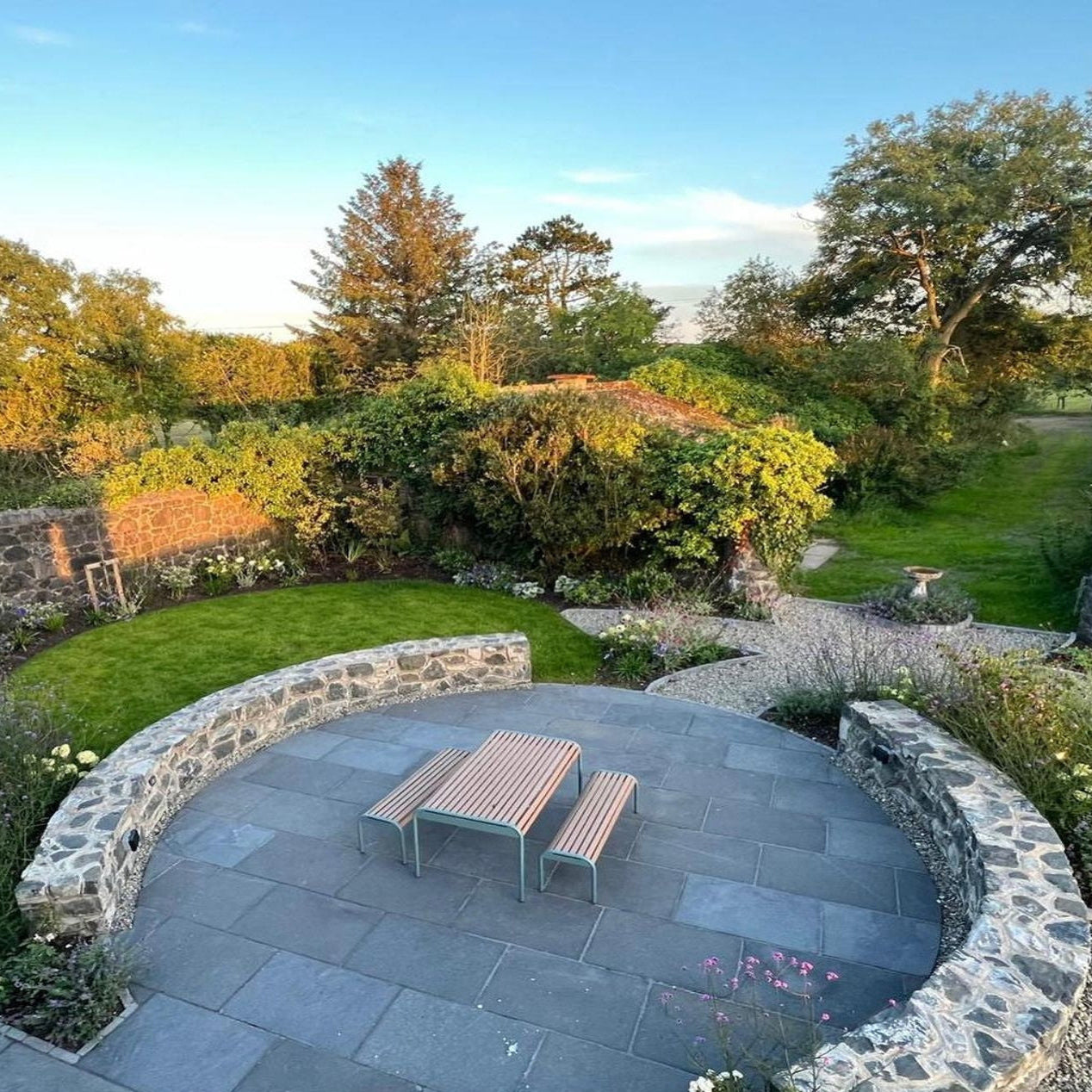 Patio area with a table and benches surrounded by greenery. Paving is Machined Black Limestone in 900 x 600mm 