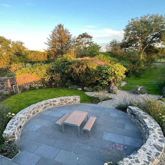 Patio area with a table and benches surrounded by greenery. Paving is Machined Black Limestone in 900 x 600mm 