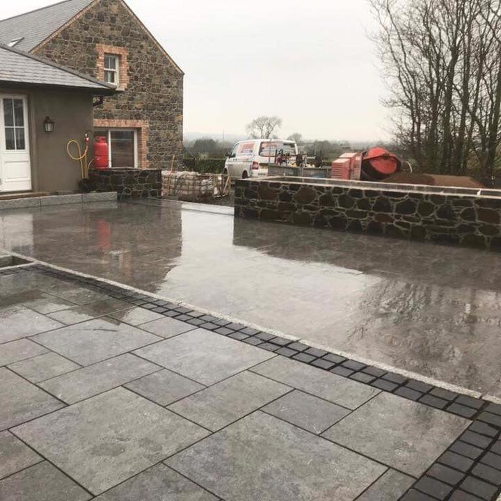 Paved patio area in front of a stone building with a cloudy sky. Patio edging is Black Limestone Paving Cobbles in 100 x 100mm